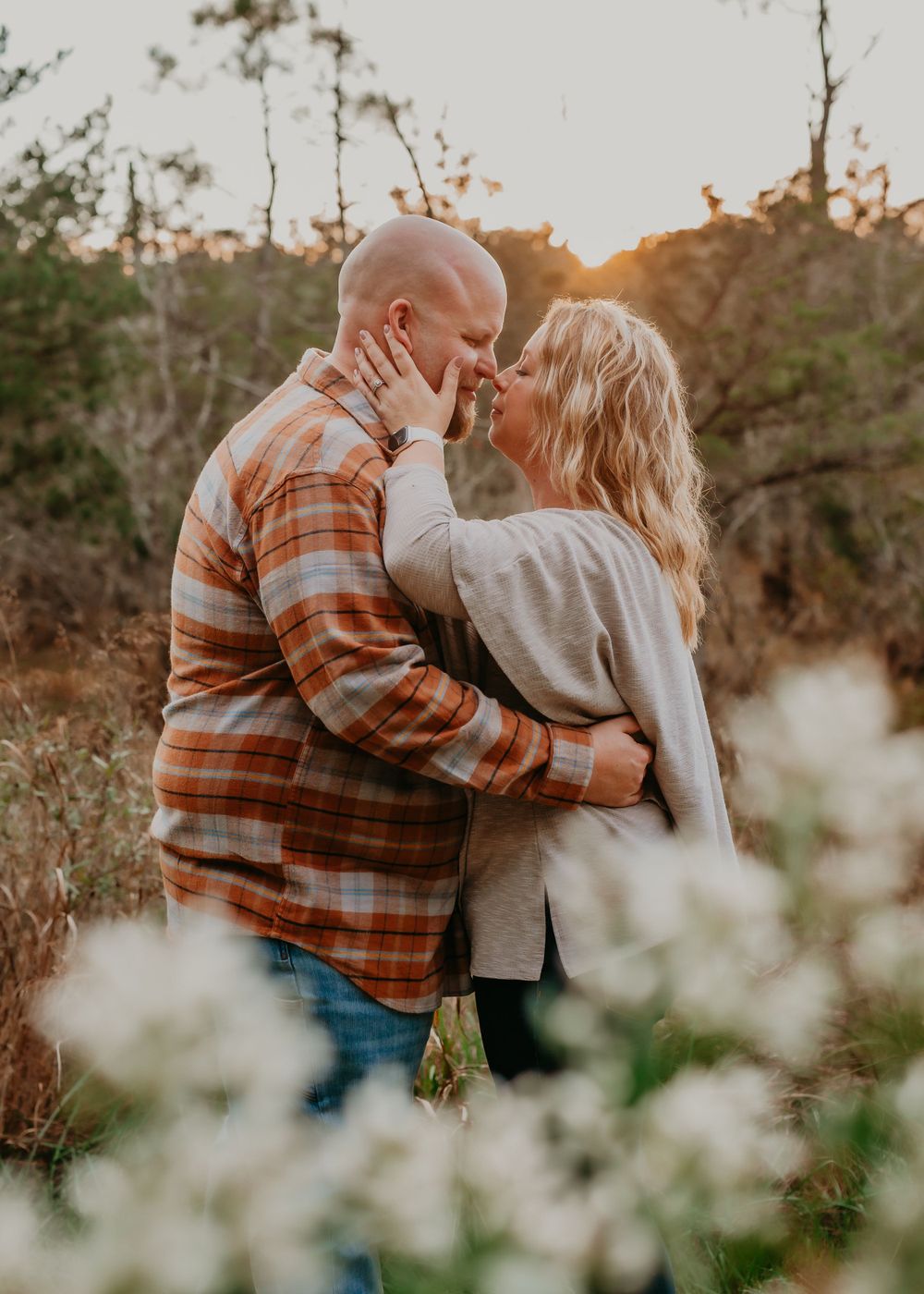 Couple sharing a romantic kiss at golden hour in a natural outdoor setting.