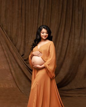 Maternity photo featuring a flowing orange dress against a brown backdrop.