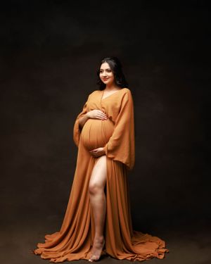 Artistic maternity portrait with flowing orange dress against moody dark backdrop.
