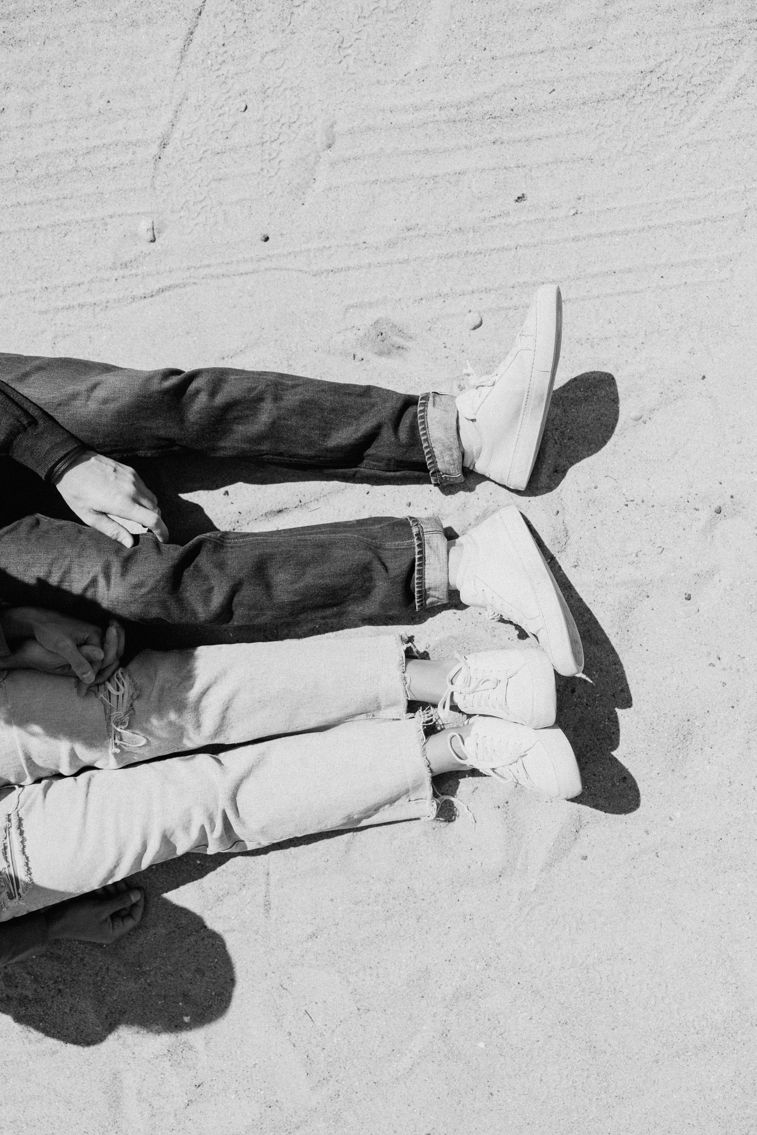 Aerial black and white photo of two people lying on sand beach showing legs and sneakers. New Bedford, Ma Miranda Photo & Co