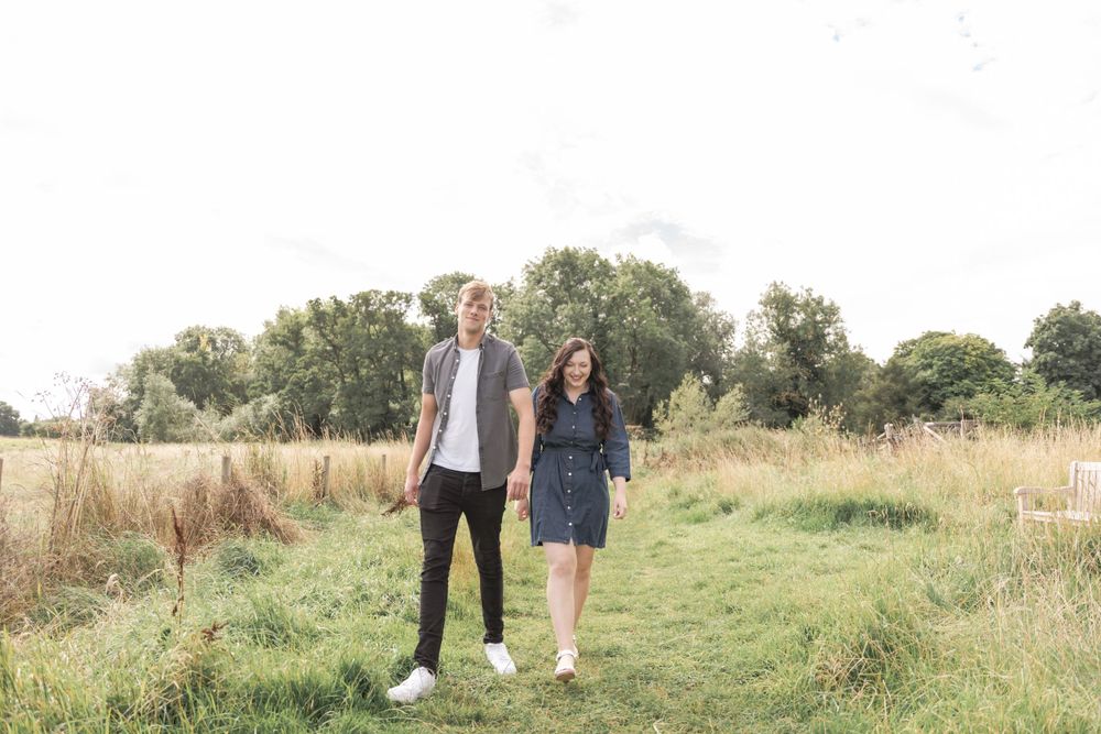 Couple strolling through a sunny meadow during a countryside photoshoot.