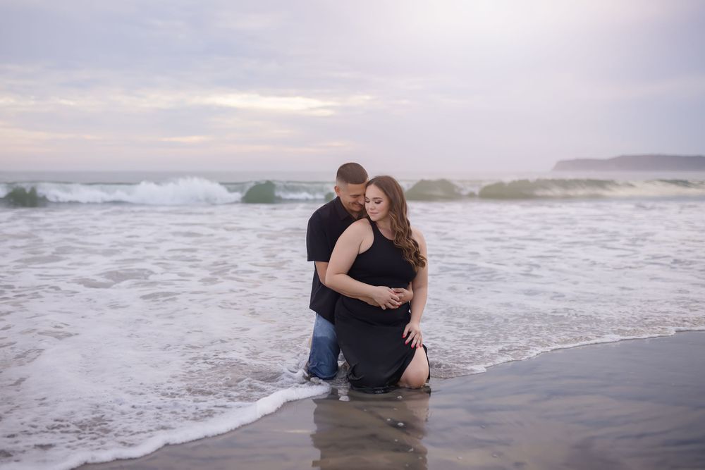 A couple embracing at the ocean's edge during sunset.