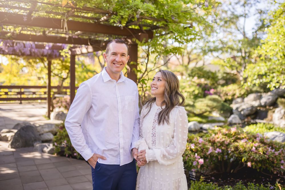 A couple shares a joyful moment in a garden setting with a wooden pergola.