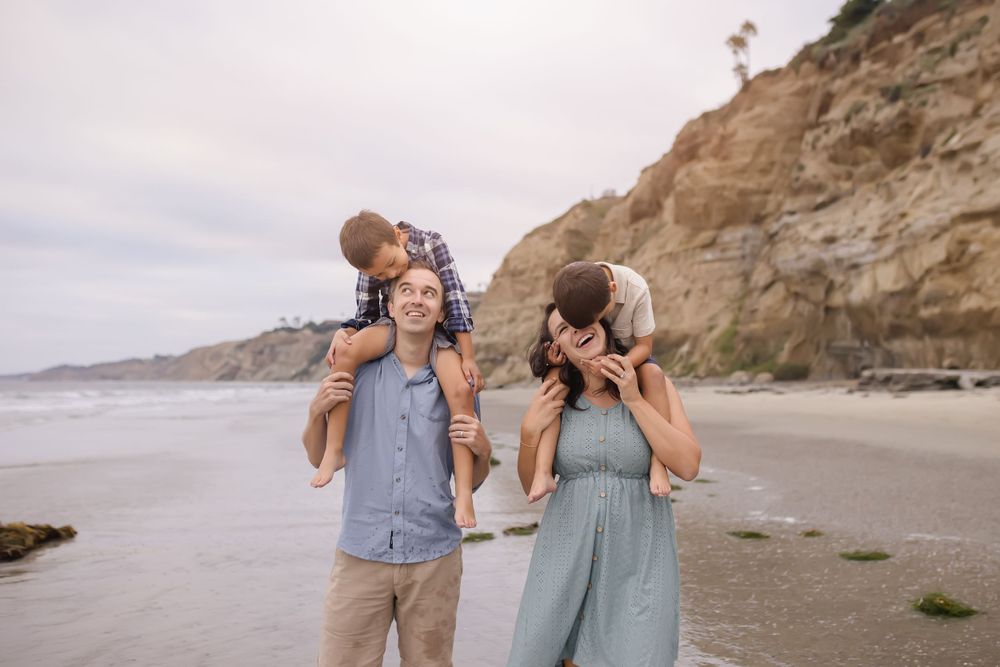Happy family enjoying a playful moment together on a scenic beach with cliffs.