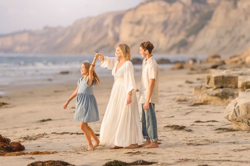Three people stand together on a beach with dramatic coastal cliffs in the background.