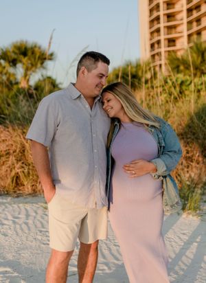 A couple shares a tender beach moment with palm trees and a high-rise building in the background.