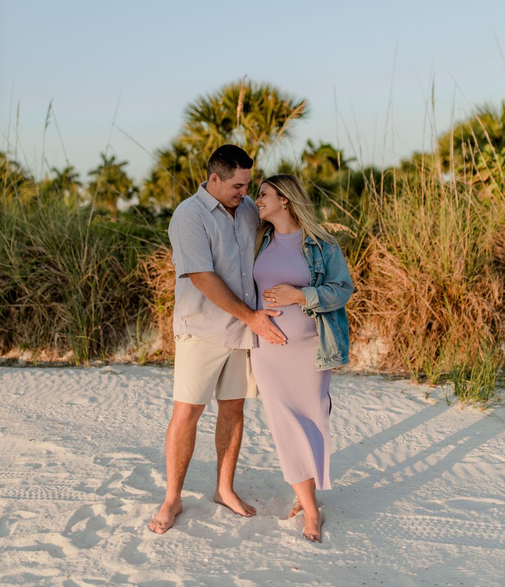 A couple stands together on sandy beach with tropical vegetation in the warm sunset light.
