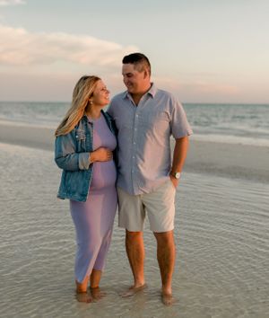 A couple embracing on the beach at sunset during a romantic maternity photoshoot.