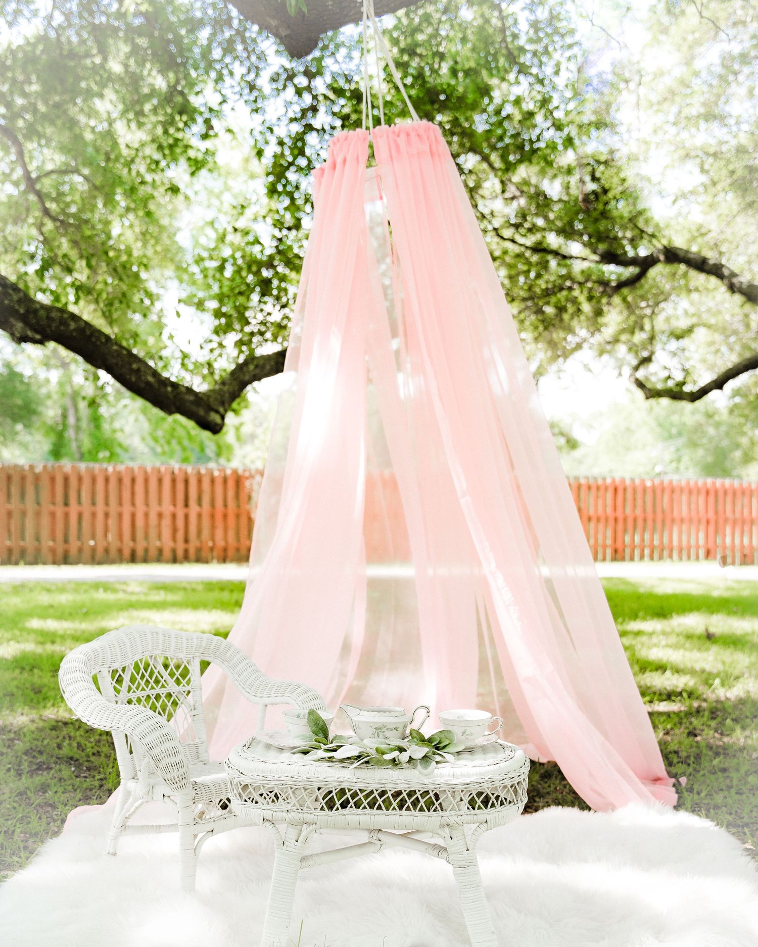 Pink canopy setup with white wicker furniture in garden setting.