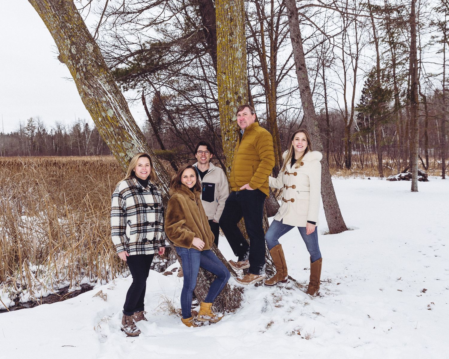 Group enjoying a winter day outdoors wearing warm coats in a snowy wooded area.