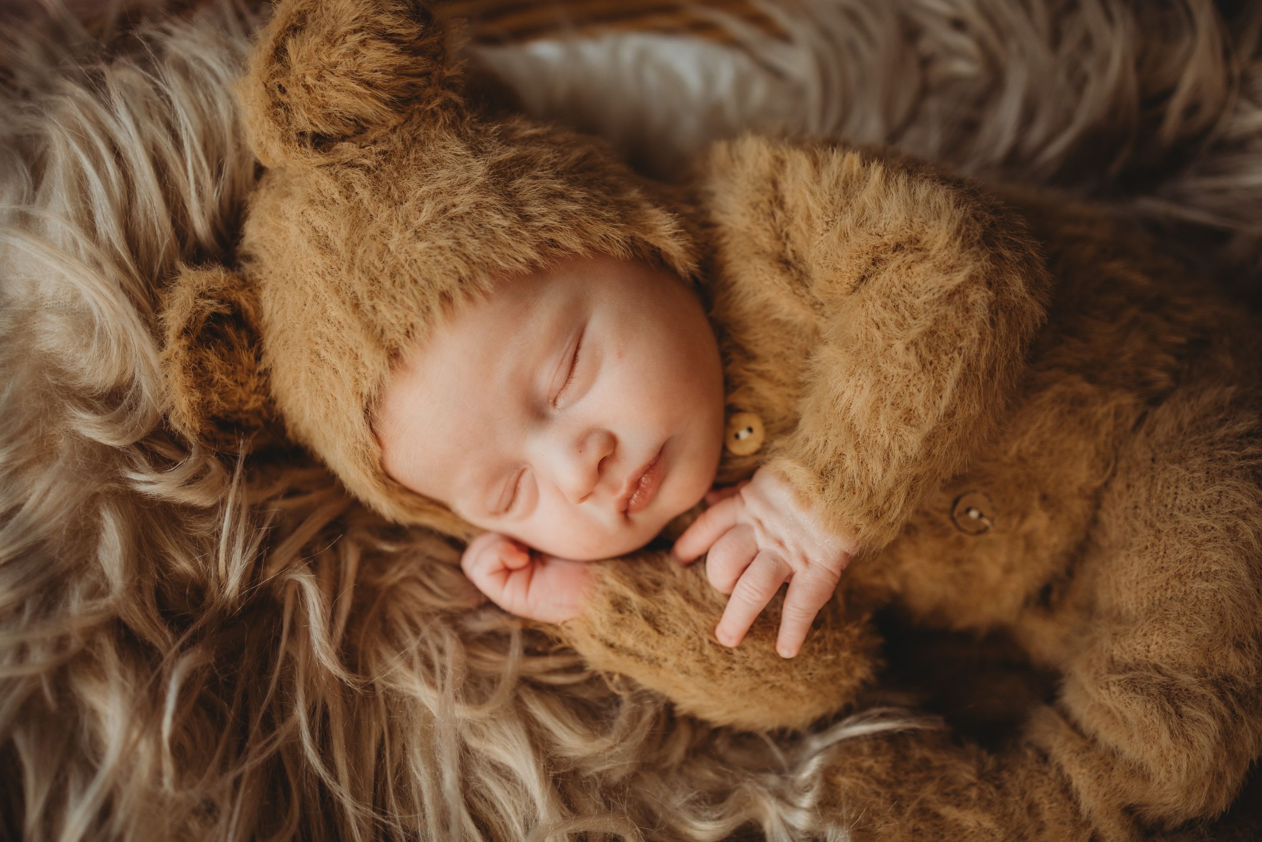 Sleeping baby wrapped in cozy brown bear outfit on furry blanket.