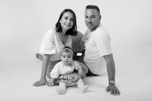 Black and white studio portrait of a family of three wearing white against light background.