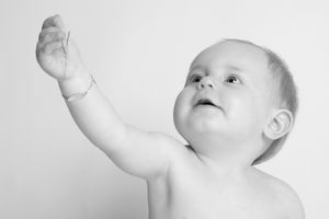 Black and white portrait of baby reaching upward against plain background.
