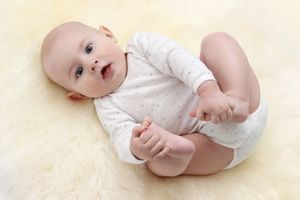 Baby wearing white onesie lying on soft yellow blanket.