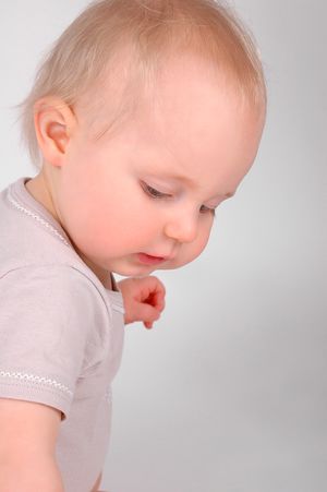 Baby in light colored shirt looking downward in profile against neutral background.