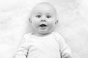 Black and white portrait of smiling baby wearing white onesie.