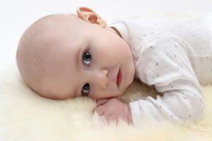 Baby in white dotted outfit lying on soft yellow surface.