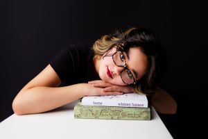 12 year old girl poses with favorite novels for birthday photoshoot with black background.