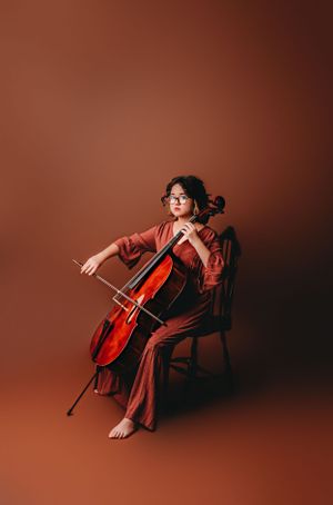 12 year old girl plays cello for birthday photoshoot in rust color dress.