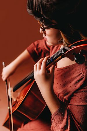 12 year old girl plays cello for birthday photoshoot in rust color dress.