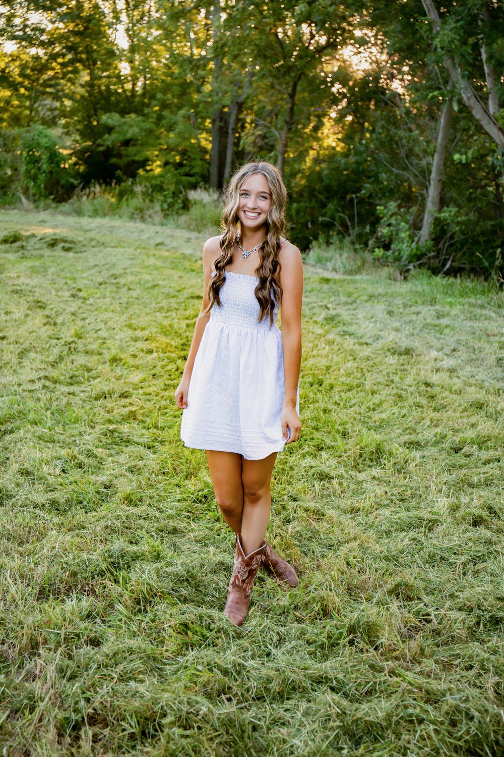 A casual outdoor portrait featuring a white summer dress and brown boots in a sunlit meadow.