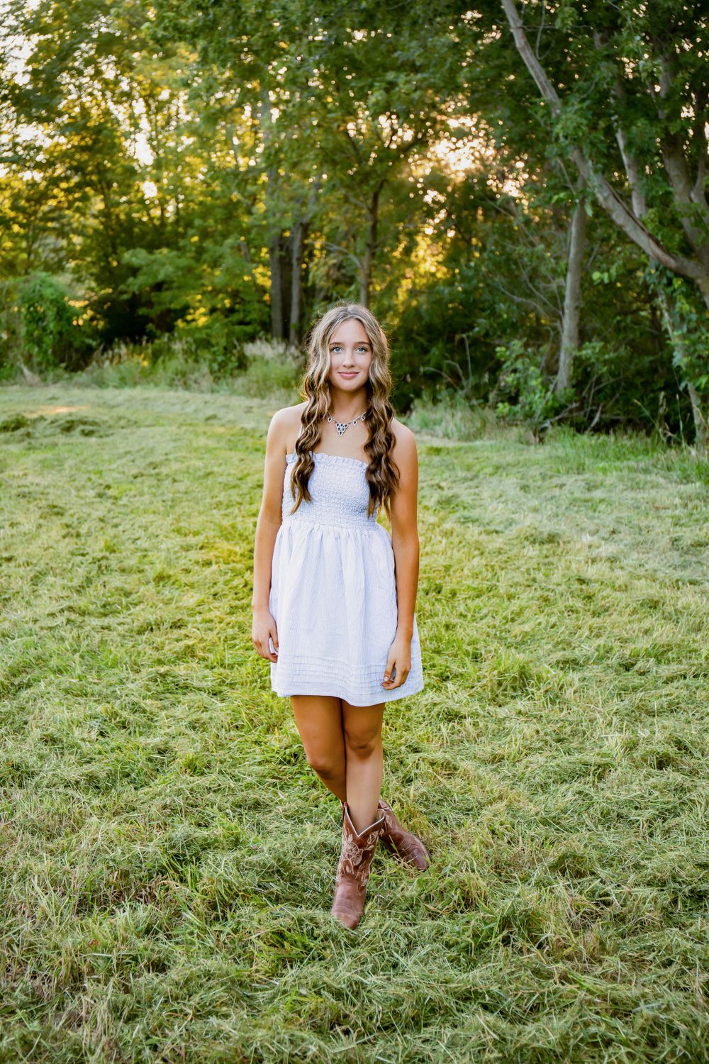 Summer portrait in white dress and cowboy boots against wooded background.