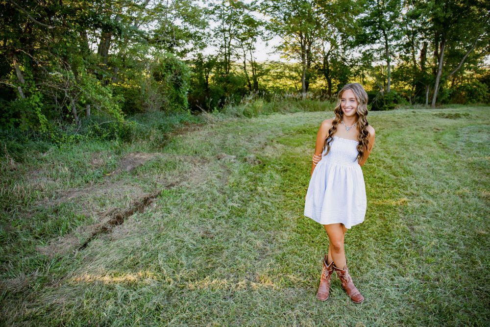 Someone in a white sundress poses gracefully in a sunlit meadow at golden hour.