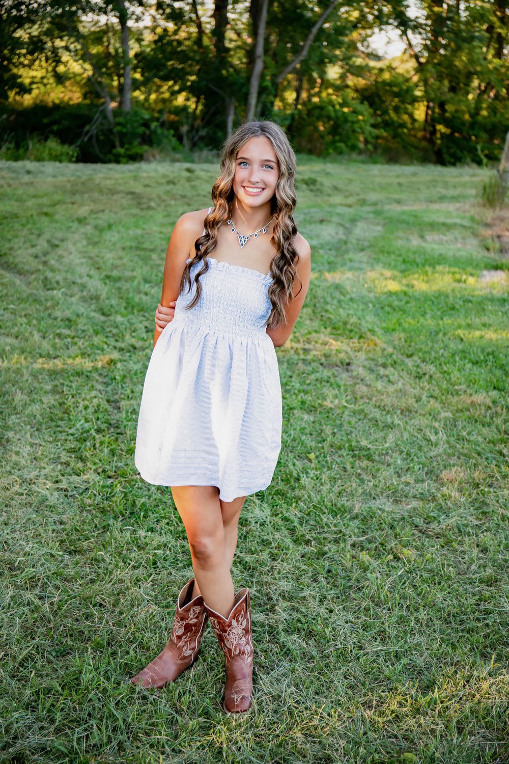 Summer portrait in a white dress and brown cowboy boots on grassy terrain.