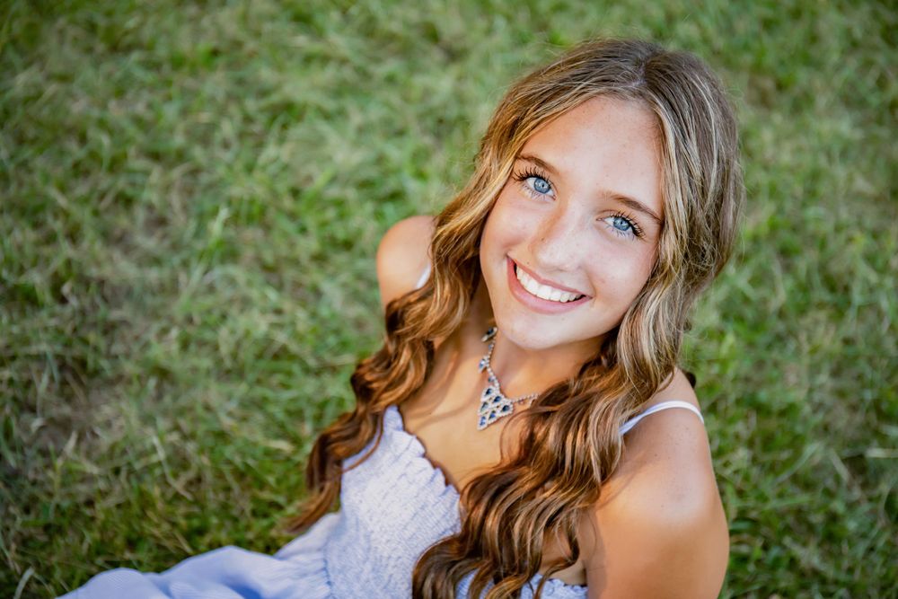 Outdoor portrait showcasing a white dress and crystal necklace against green grass.