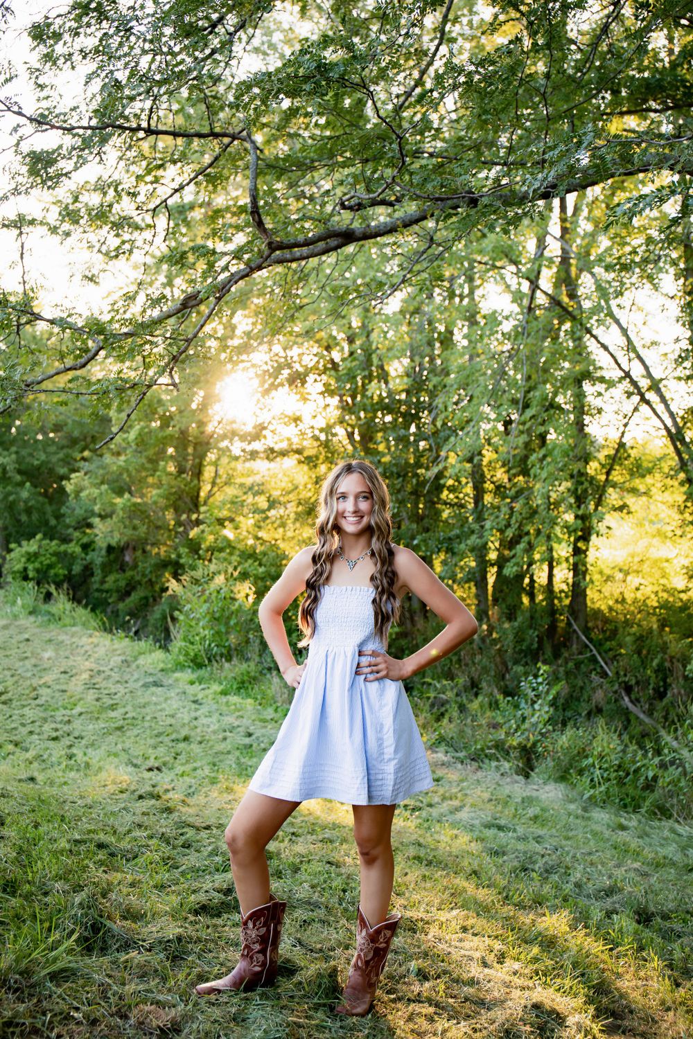 Golden hour portrait under tree branches wearing a white dress and cowboy boots.