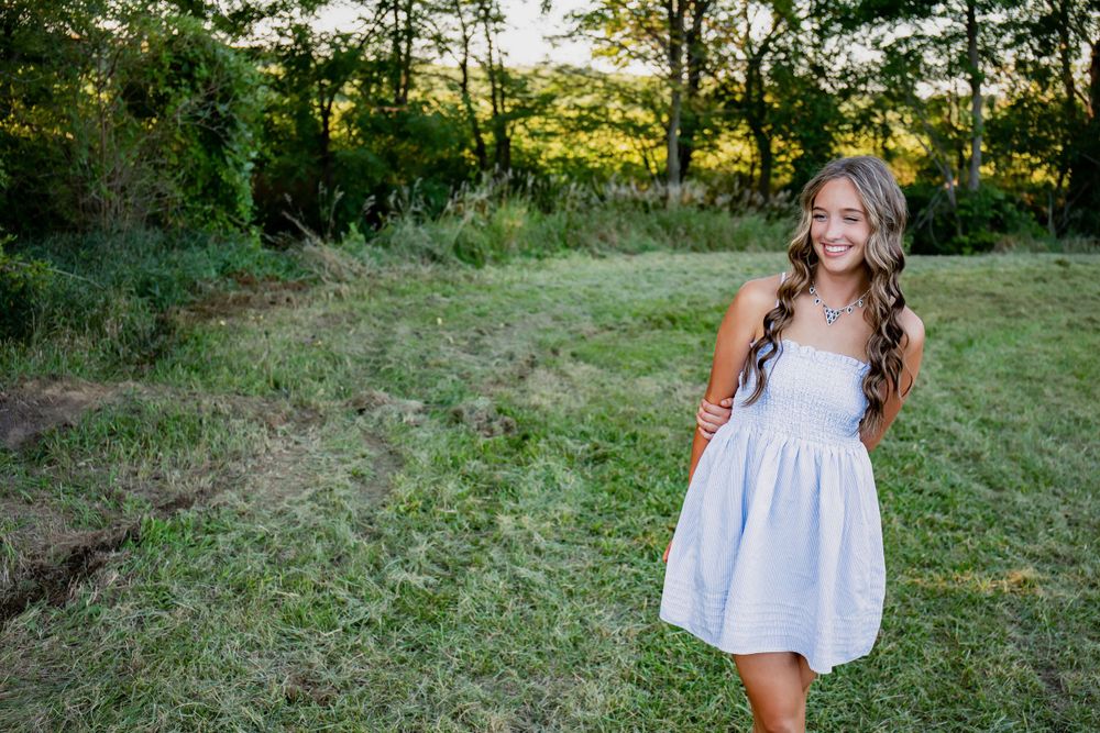 Person in a light summer dress stands in a grassy field during sunset.