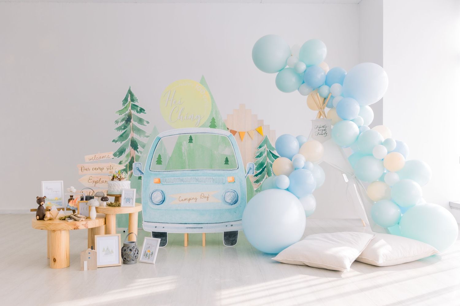 Whimsical baby shower setup with blue balloon arch, vintage car backdrop and wooden decor elements.