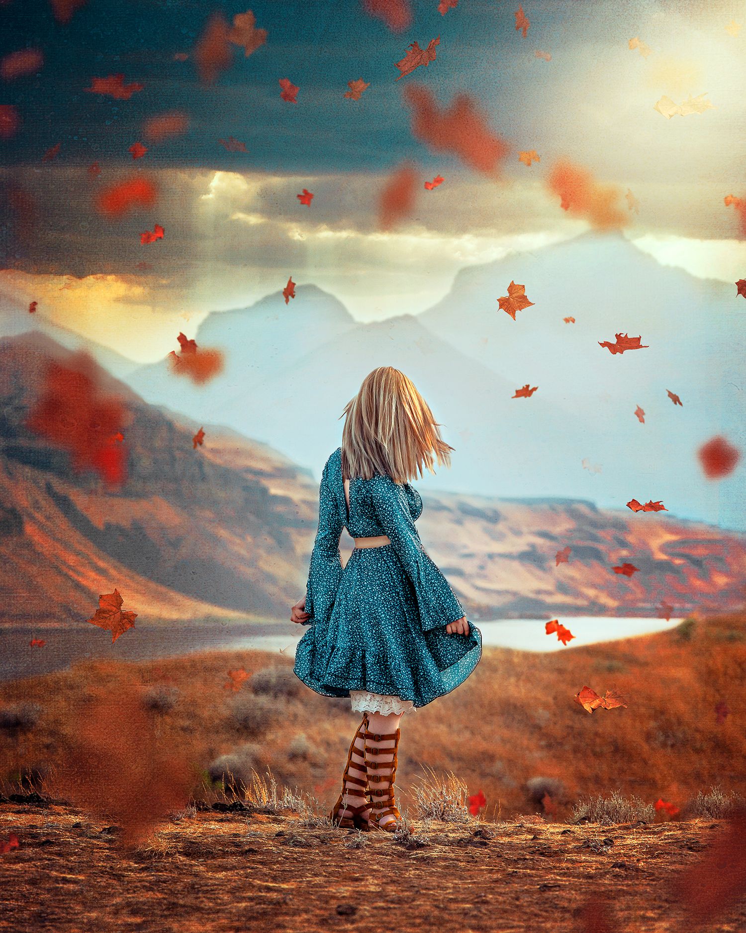Blonde girl in dress standing on cliffs edge with autumn leaves blowing around her