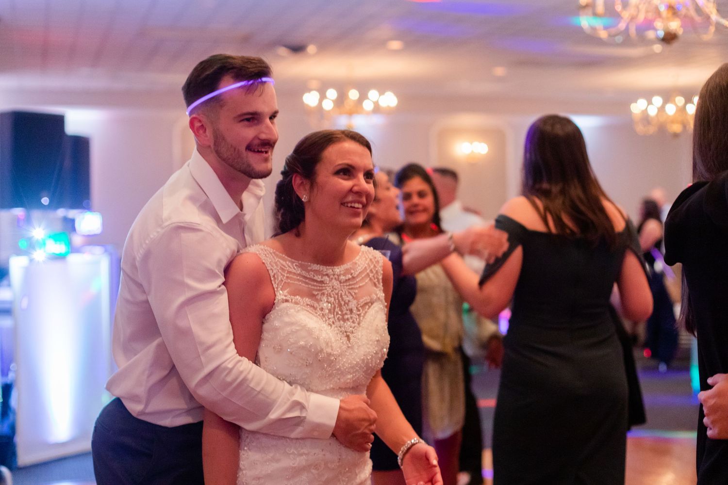 Couples dancing together at an elegant wedding reception with blue lighting and chandeliers.