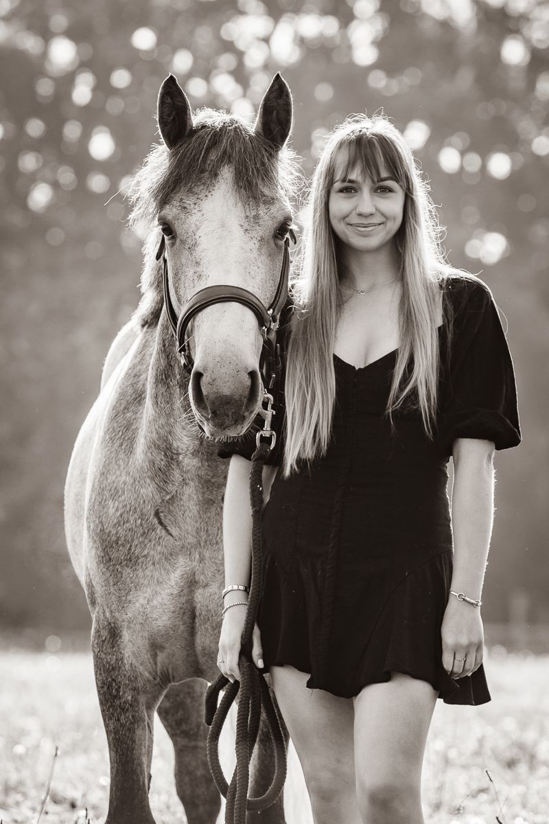 A dappled grey horse stands close to their companion in black and white portrait style.