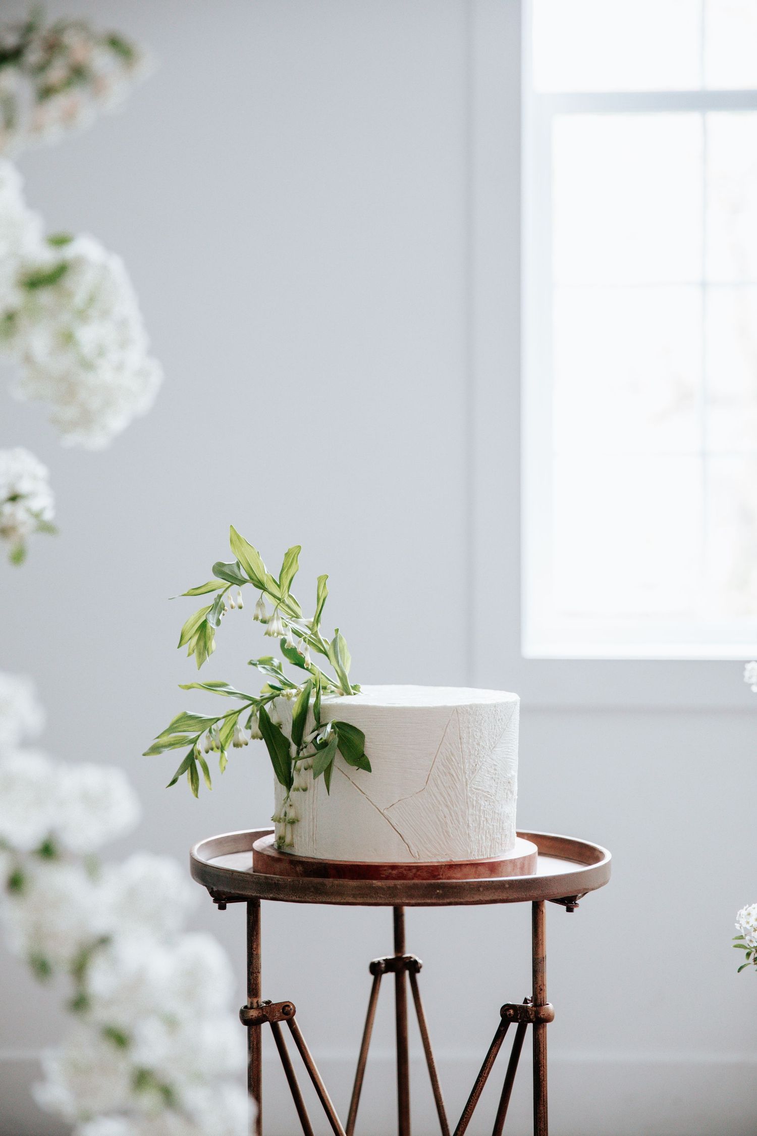 Elegant white wedding cakes displayed on wooden stands in a bright minimalist setting.