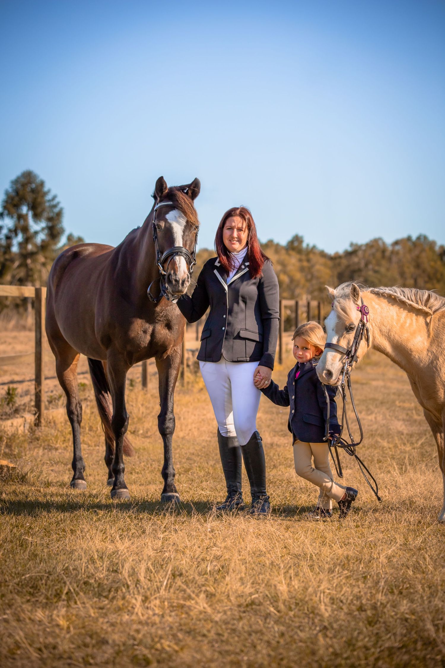 A mother and her young daughter stand facing the camera holding their two horses next to them
