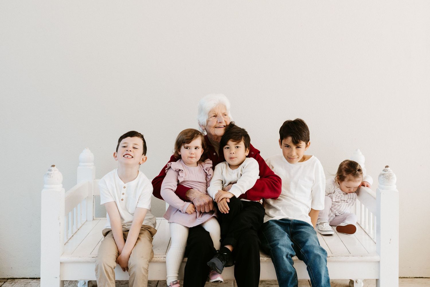 A multi-generational family sits together on a white bench for a casual portrait session.