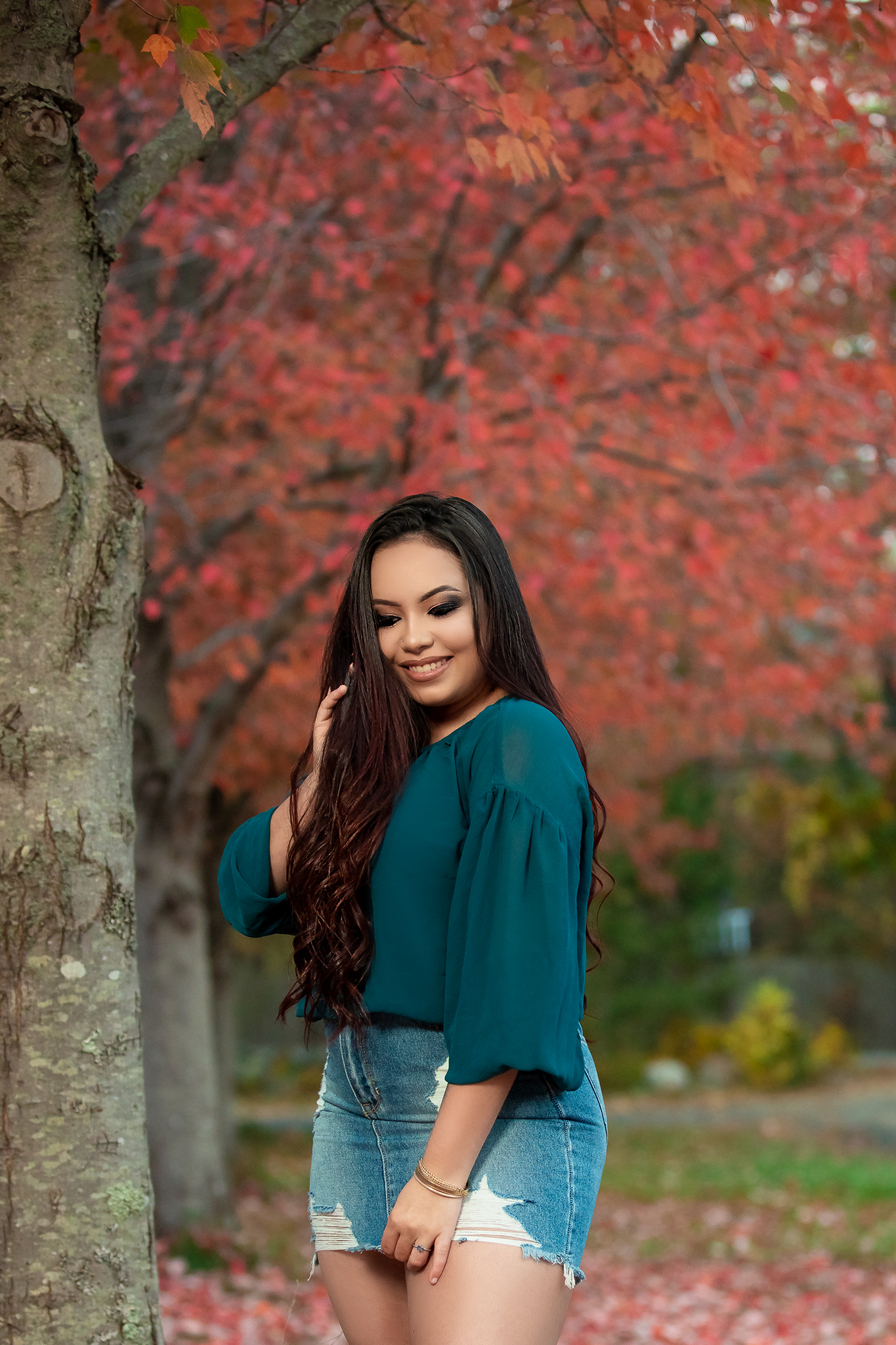 Person in teal top poses beneath vibrant red autumn foliage.
