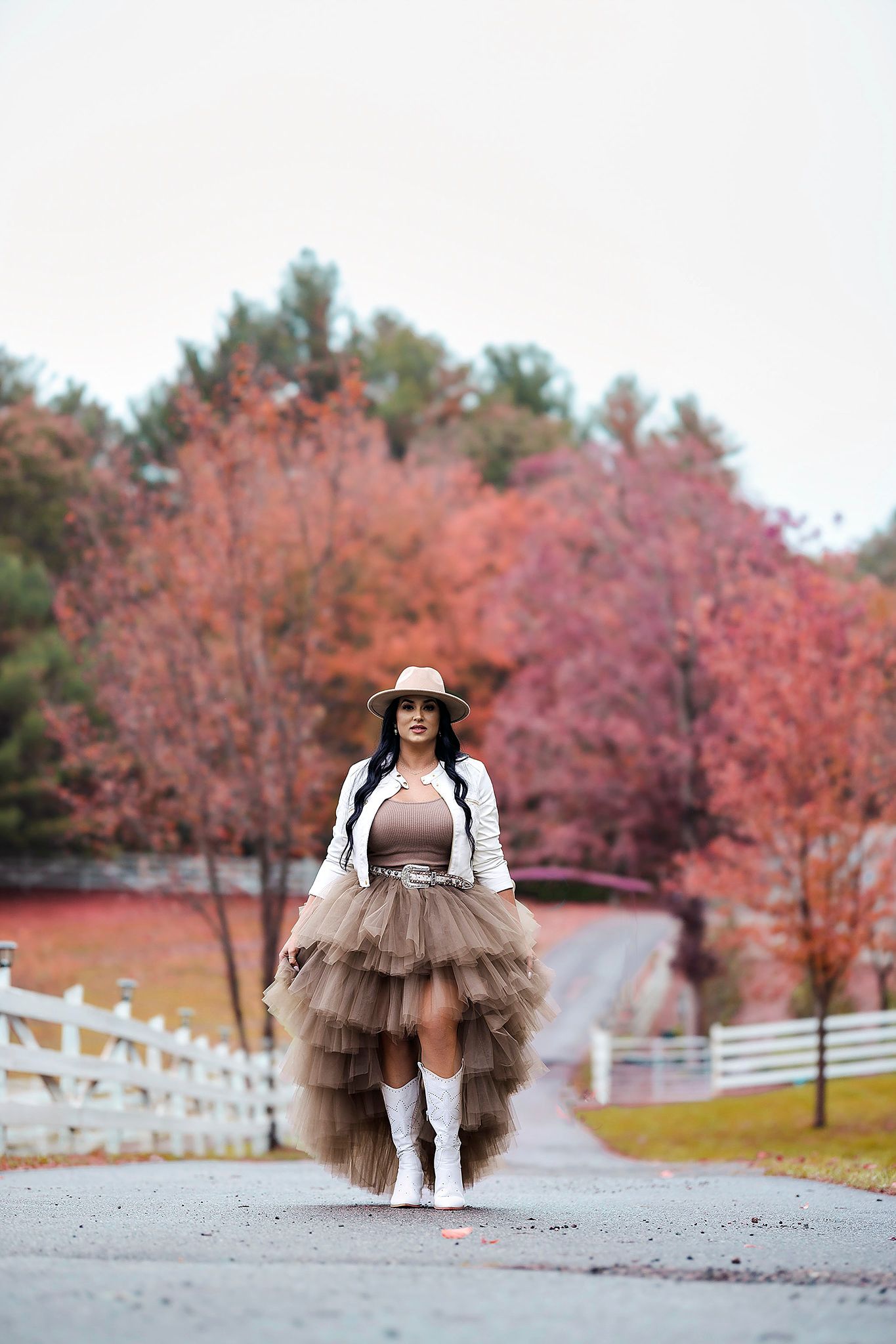 Whimsical photoshoot featuring brown tulle dress against fall foliage and white fence backdrop.