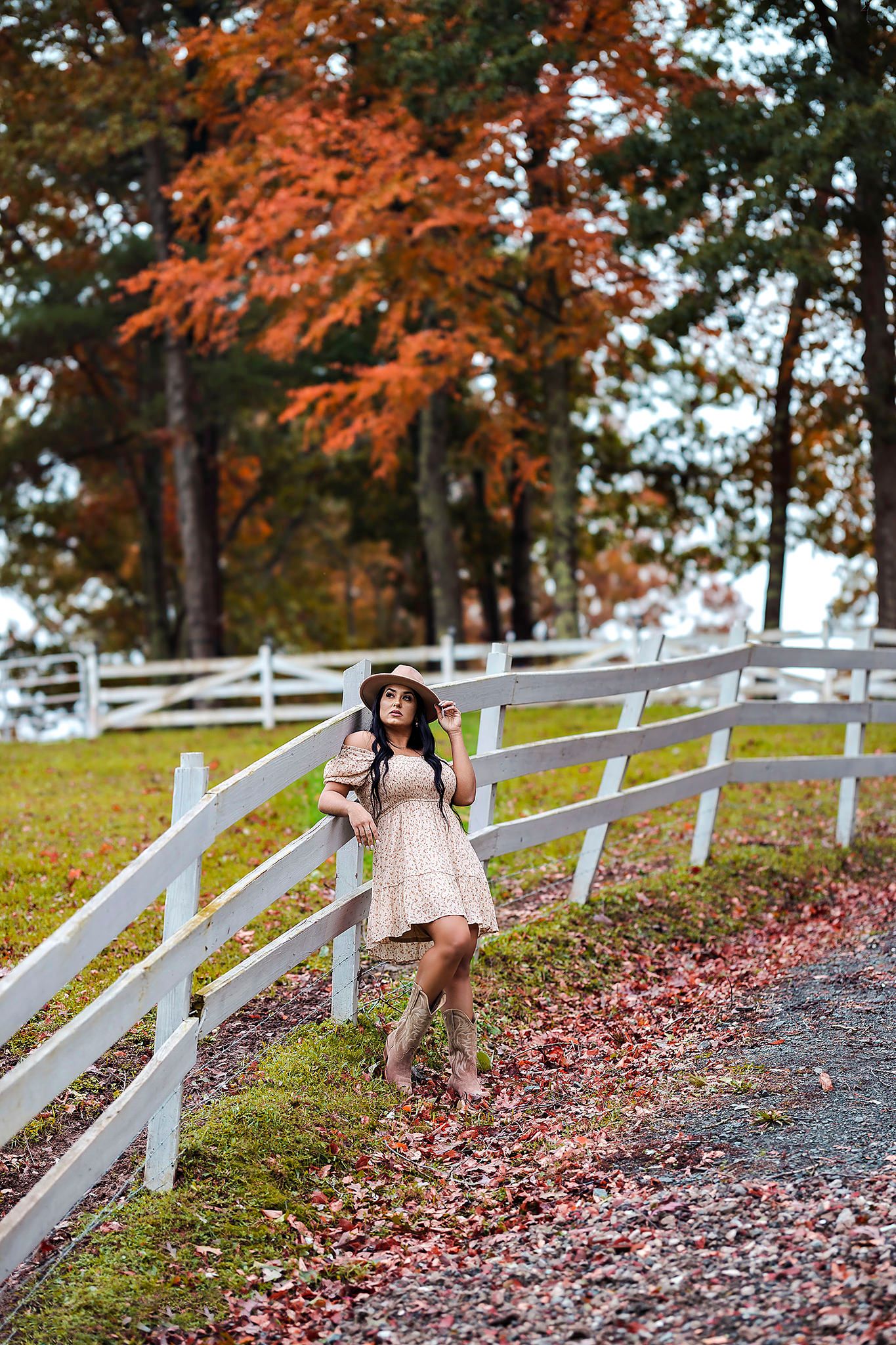 Rustic autumn photoshoot along white fence with falling leaves and warm lighting.
