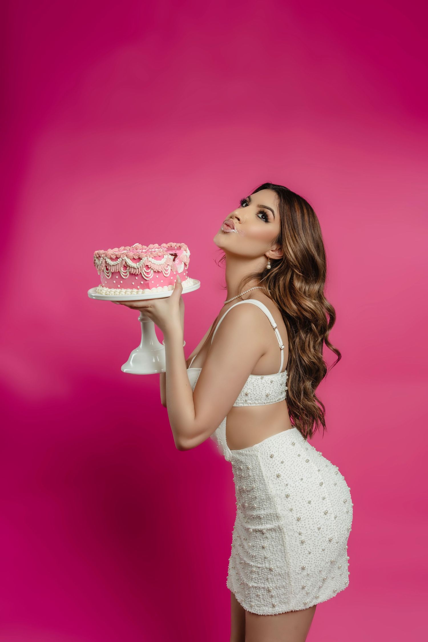 Whimsical cake smash photo series against bright pink background in white dress.
