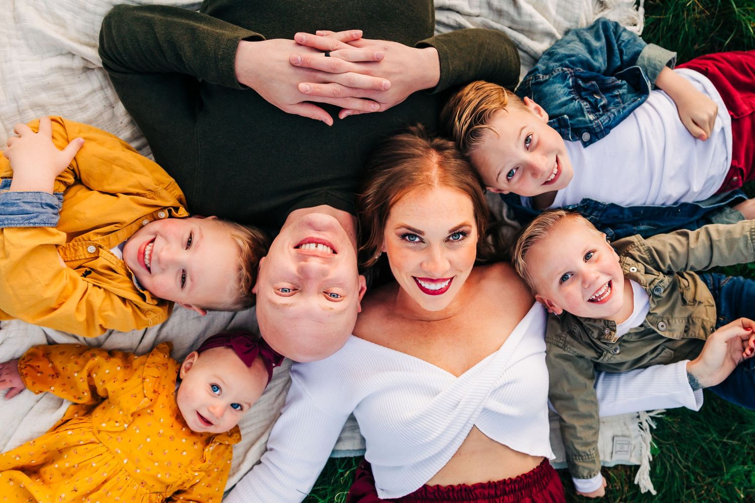 Family lying on blanket with children in casual outdoor portrait session.