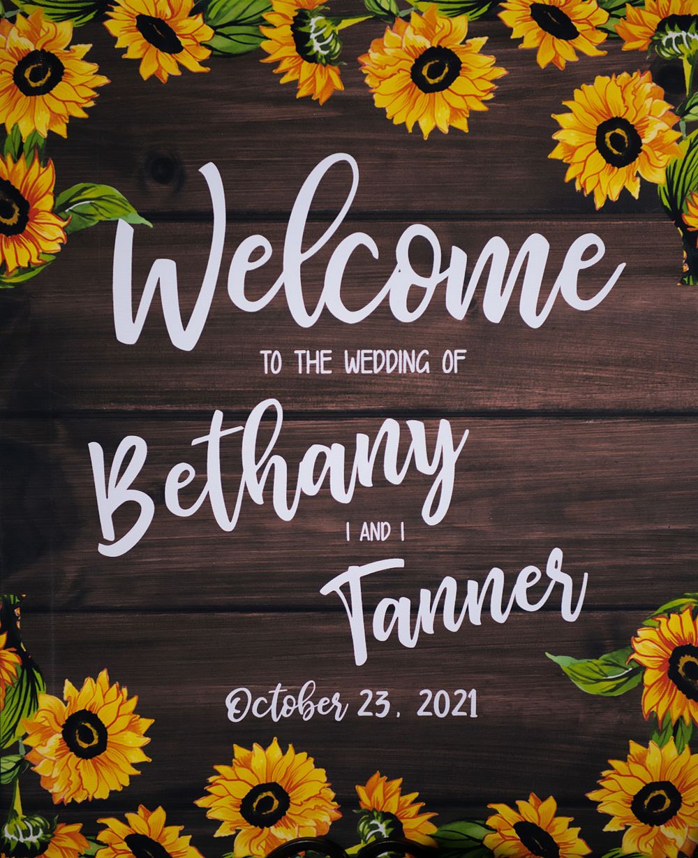 Rustic wooden wedding welcome sign decorated with painted sunflowers.
