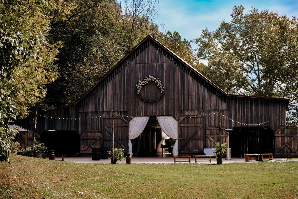 Rustic wooden barn decorated for a wedding ceremony with white curtains and chairs on a sunny autumn day.