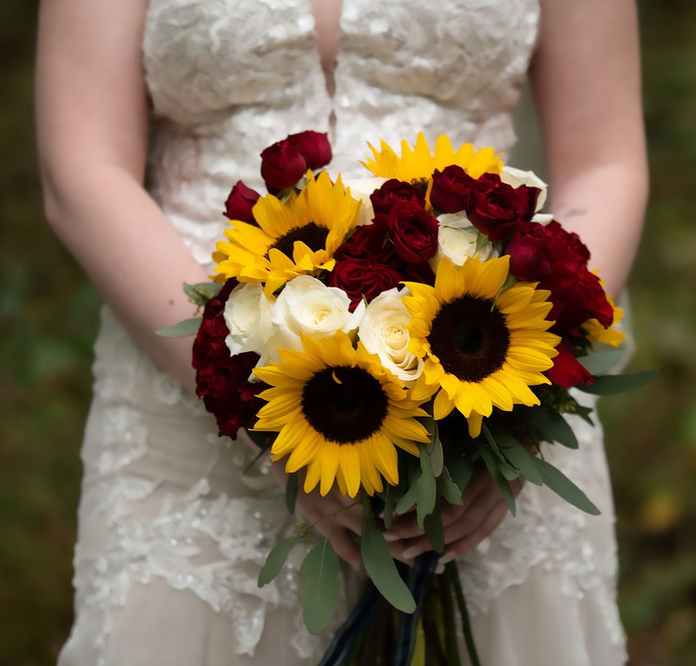 Wedding bouquet featuring vibrant sunflowers and deep red roses wrapped with a dark ribbon.