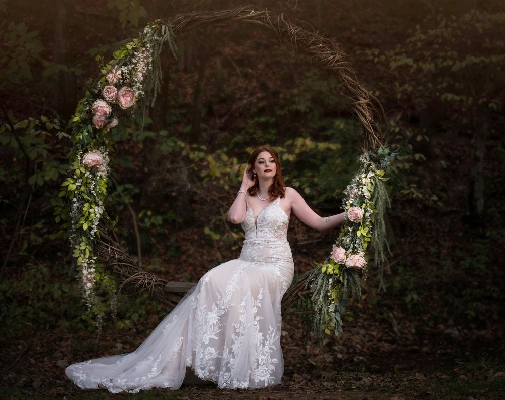 Wedding dress portrait under a floral arch in an enchanted forest setting.