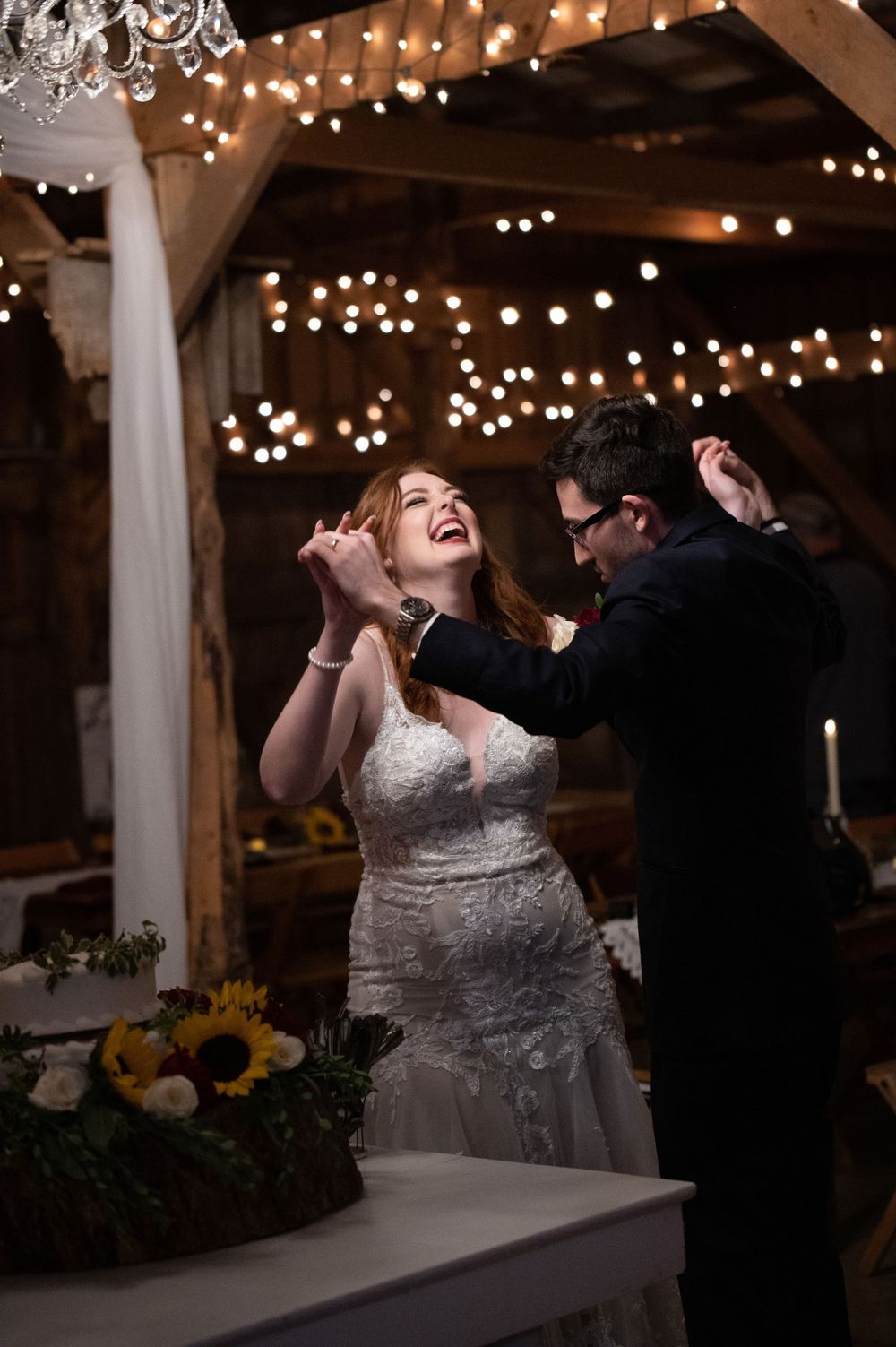 Joyful couple dancing under twinkling lights at their rustic barn wedding reception.