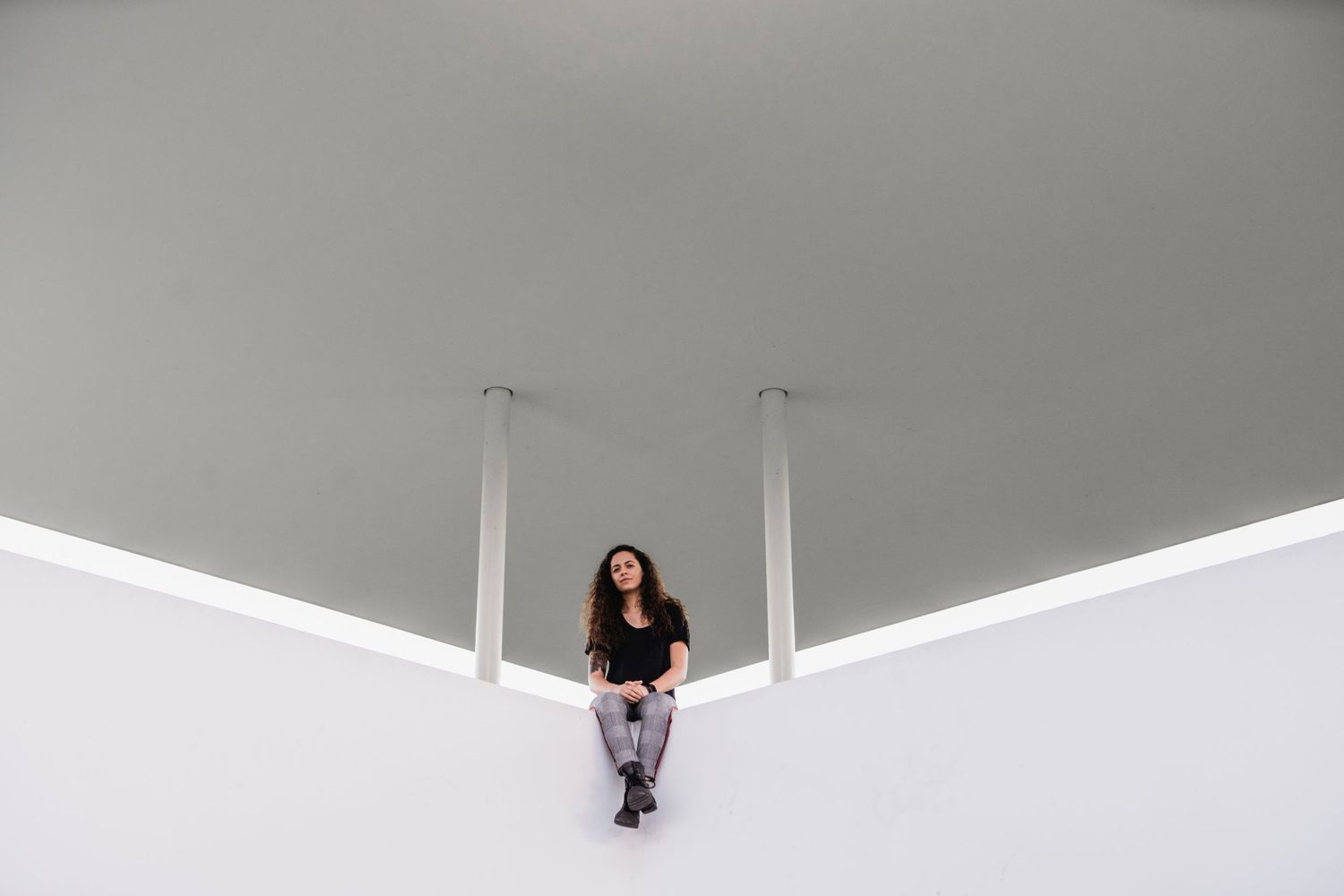A person sits centered between two white columns beneath a minimalist architectural overhang.
