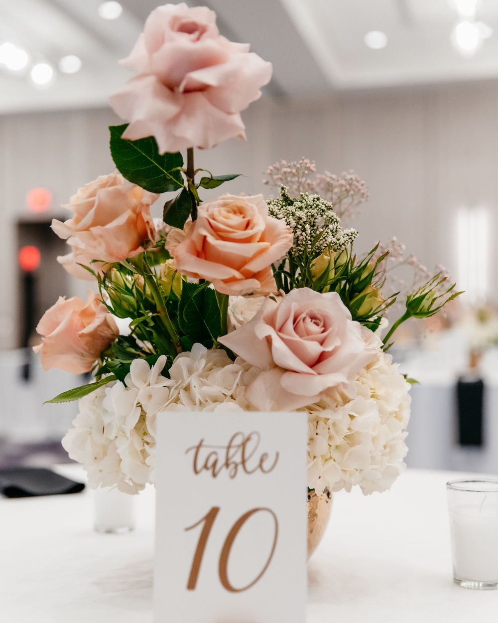 Wedding table number 10 surrounded by pink roses and white hydrangeas in elegant centerpiece.